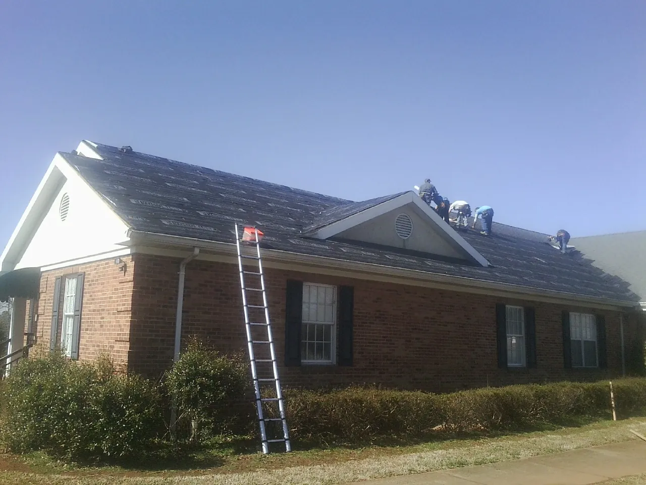 Crew tearing shingles off a brick ranch roof with a ladder set — Metal Roof Repair work by our crew in Phillipsburg