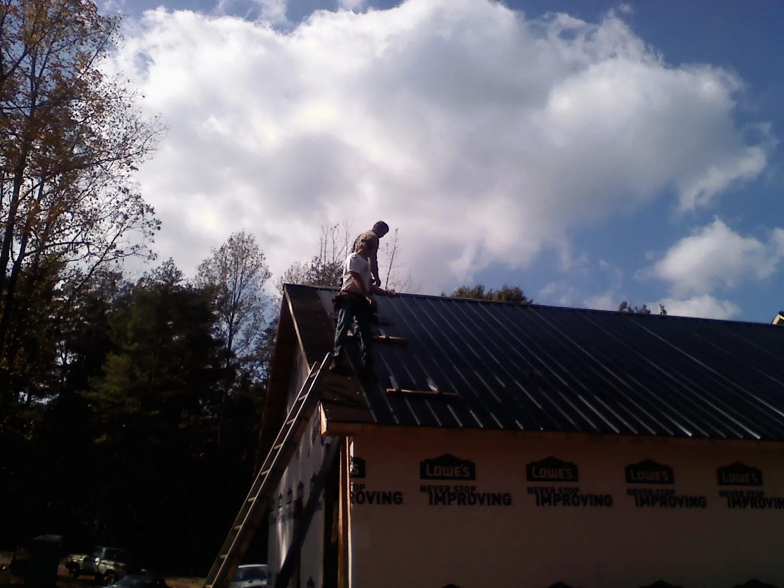 Roofer fastening dark metal panels high against a cloudy sky, from a Roof Inspection job in Phillipsburg
