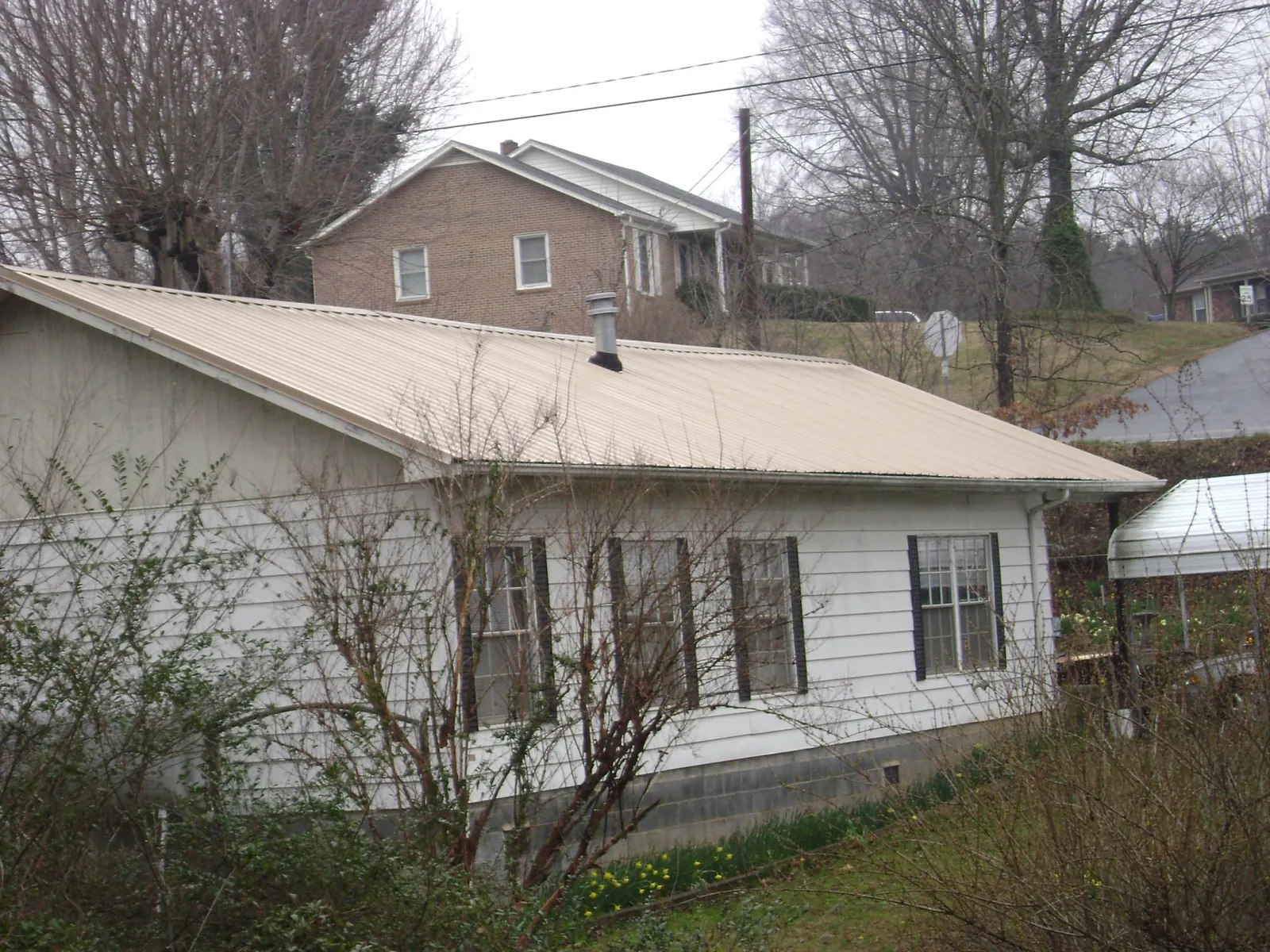 Tan metal roof on a white sided house set into a hillside in Phillipsburg